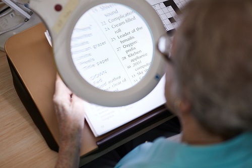 An older women uses a desktop magnifier to read a crossword