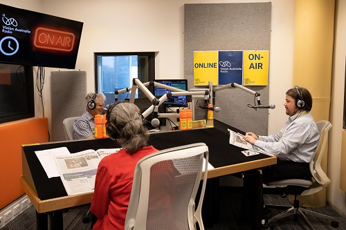 Three people sit in a radio studio behind microphones