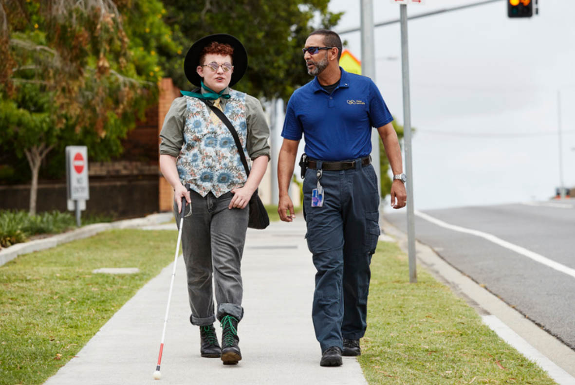 Someone learning to use a white cane alongside a Vision Australia worker.