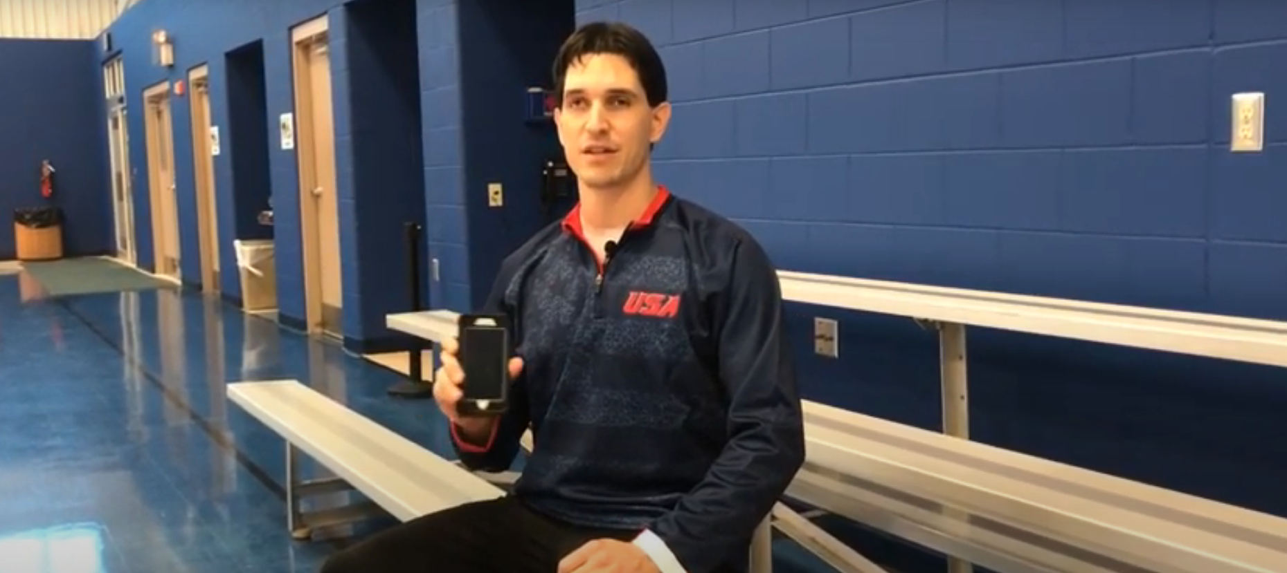 Tyler Merren holding an iphone in a gym.