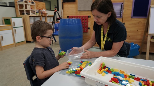 A young boy uses LEGO Braille under supervision from a Vision Australia staff member