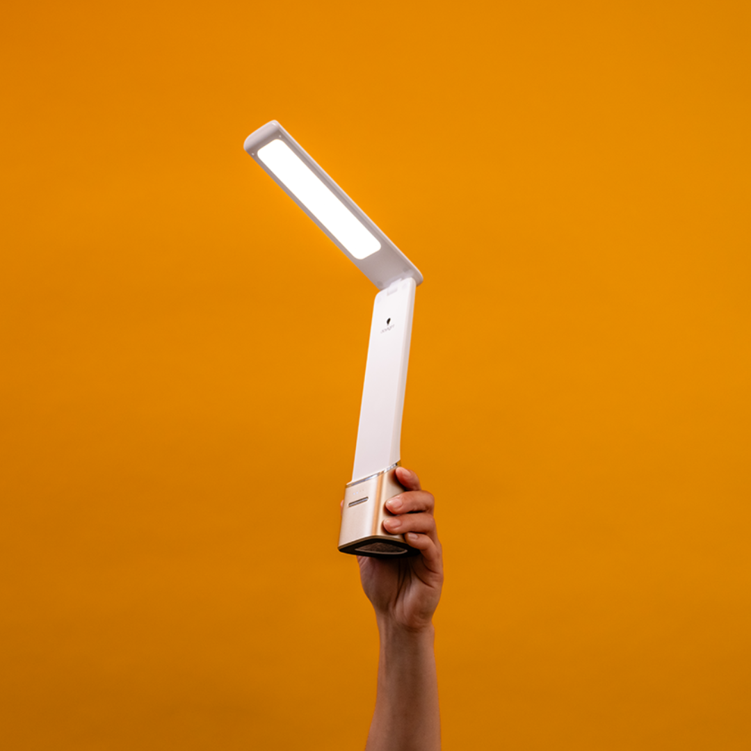 Someone holds a modern portable lamp against an orange background. 