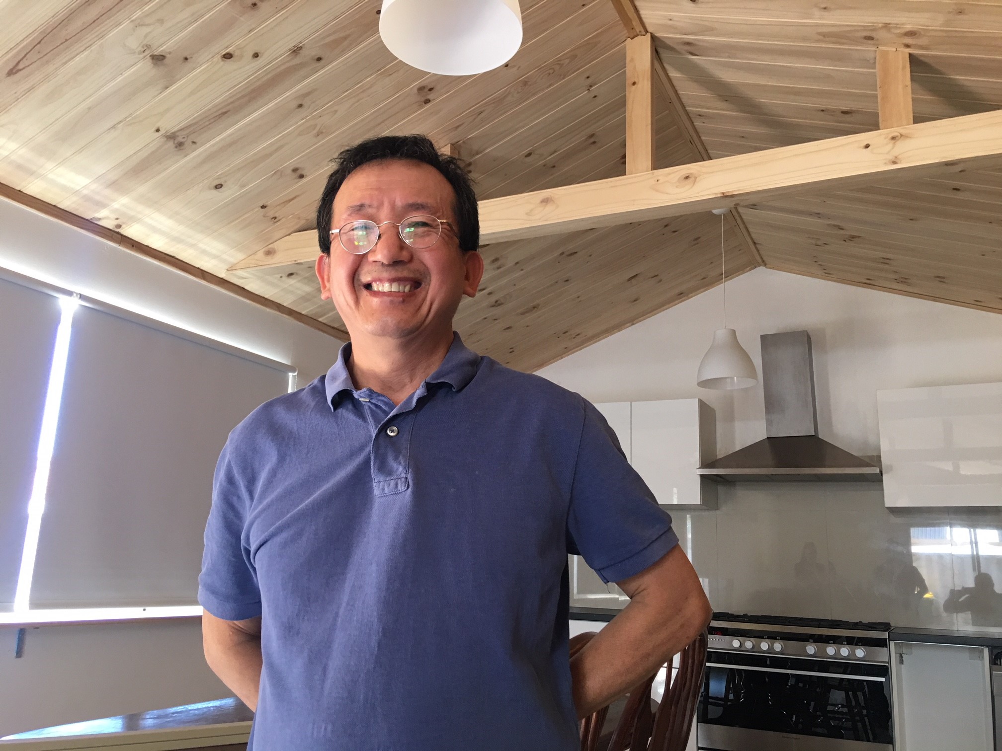Dr Ba Huynh Pham smiling at his timber-lined ceiling in a room in his home