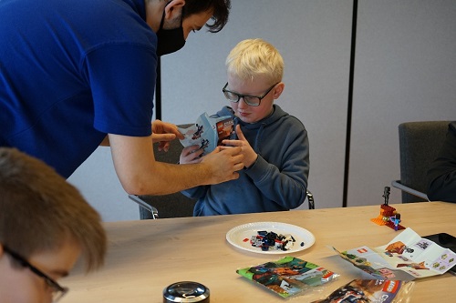 A young boy holds a Lego kit under the guidance of a man