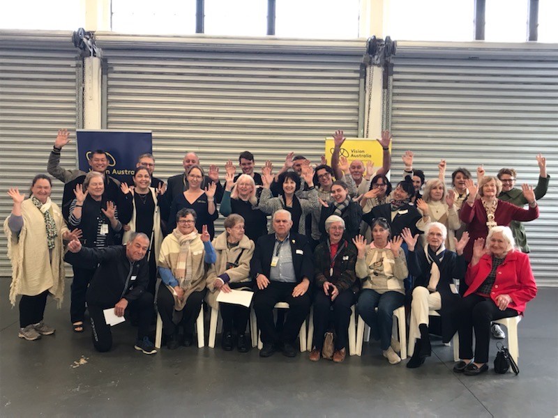 A group of around 30 Perth Vision Australia Radio volunteers smiling and waving 