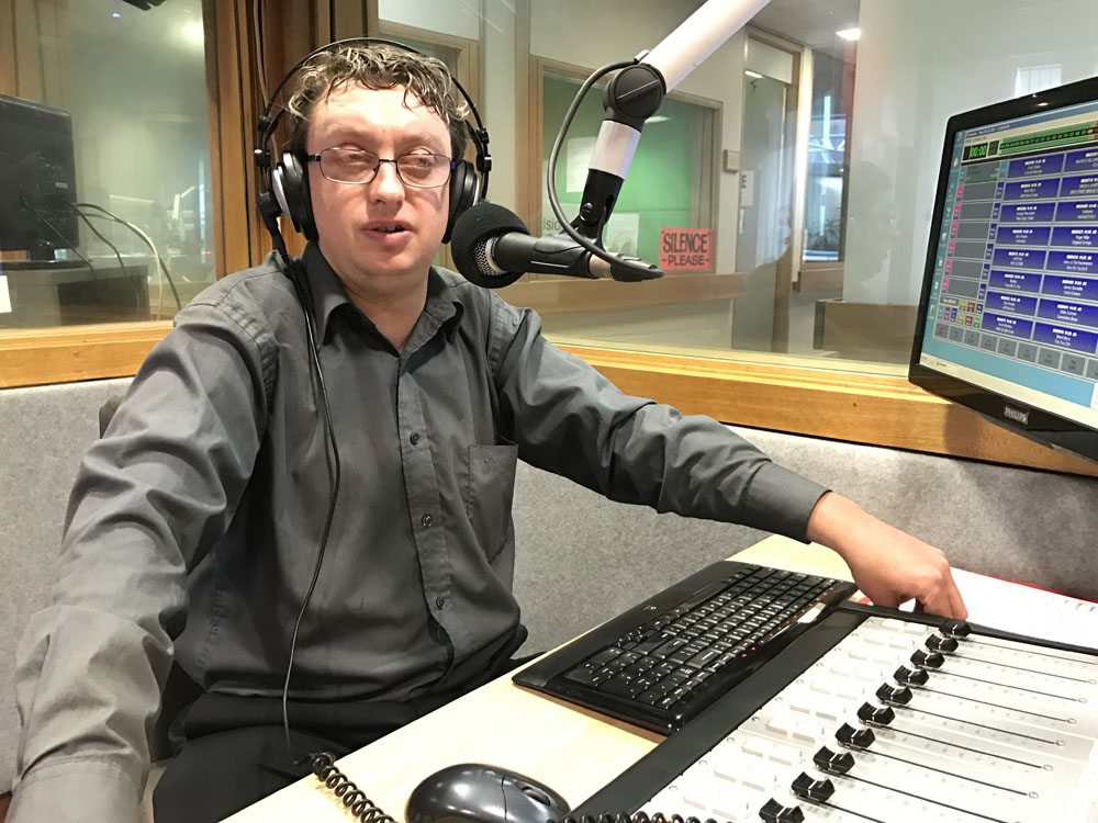 A man sits behind a microphone in a radio studio