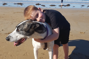 Zavier is happily hugging his dog whilst at the beach