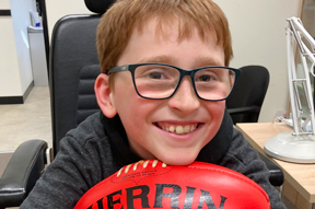 Zavier is smiling at camera and holding an AFL football