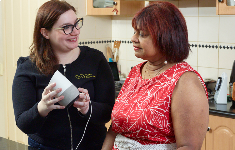 Vision Australia staff member demonstrates a Google Home device to a woman in her kitchen