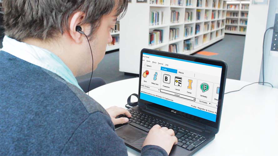 A man with a laptop sitting at a table in a library running Dolphin ScreenReader