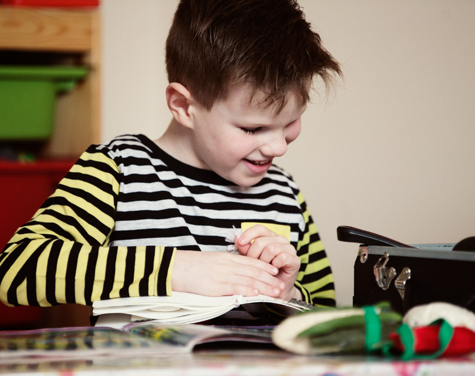 Max is smiling whilst reading a book with braille