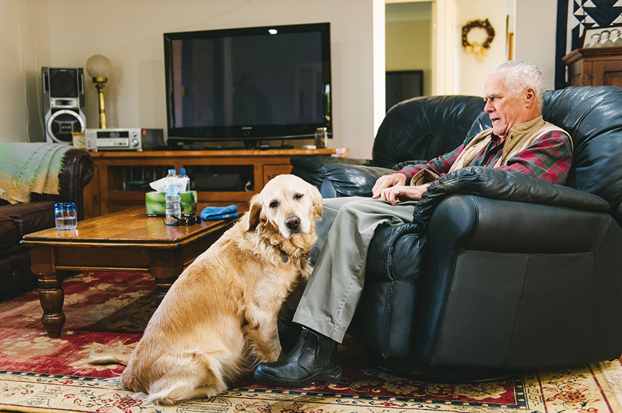 David sits in his lounge chair at home with Zahra sitting next to the lounge chair