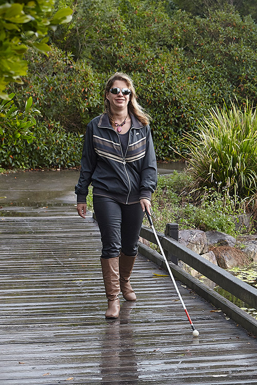 Nicole walks along a path in a park using her white cane