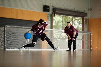 Alison in her QLD uniform rollls a goalball as her coach watches on