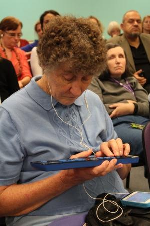 Photo of Coral sitting in audience using a braille display