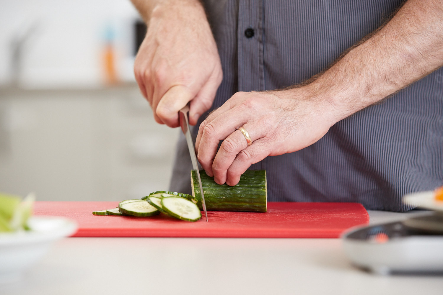 "Close-up shot of a person's hand as they chop up some cucumber"
