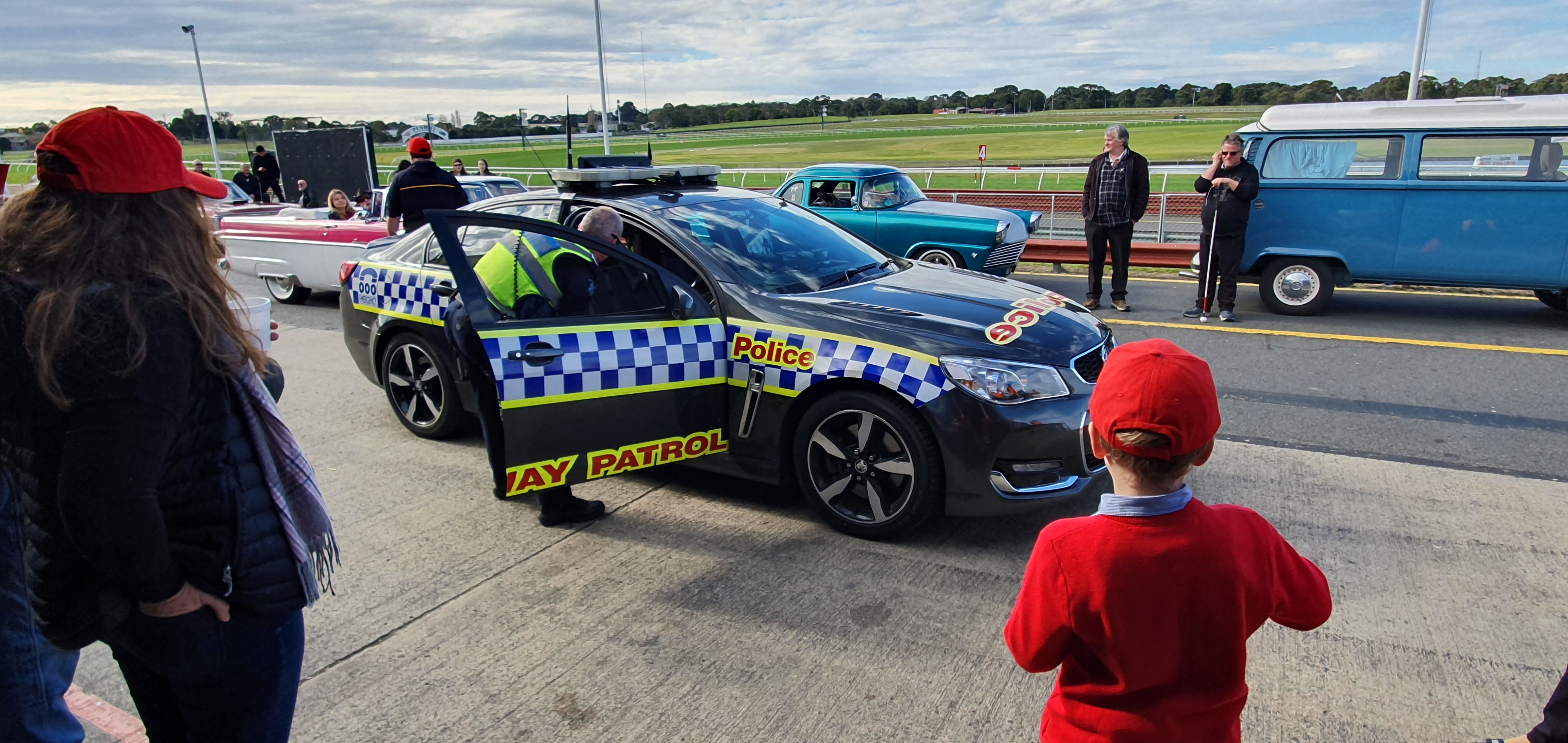 "A police car on the Sandown Racecourse with a police officer looking into the car."