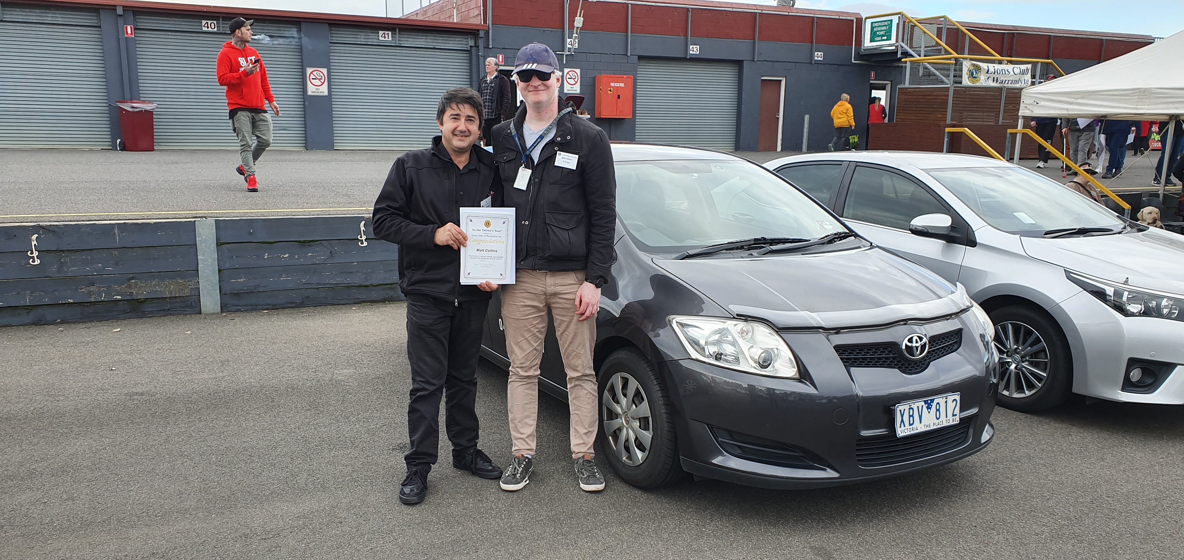 "The driving instructor and myself stand next to the car I drove as he presents me with a certificate commemorating the day."