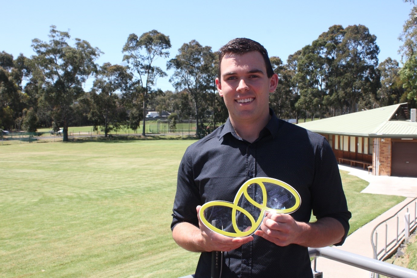 "VA Award winner Ben, holding his award which takes the shape of the VA logo of 3 yellow ovals linked together.]"