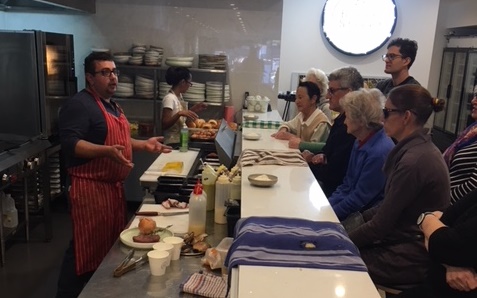 Chef Daniel giving instructions to the assembled group inside the kitchen of his restaurant