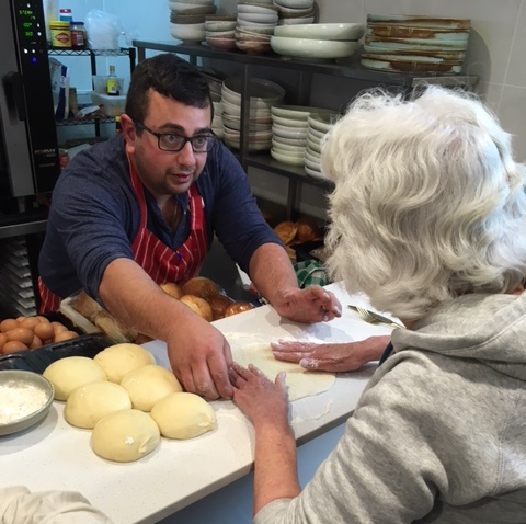 Chef Daniel talking with a Vision Australia client, rolled up mounds of pizza dough are on the board in front of them
