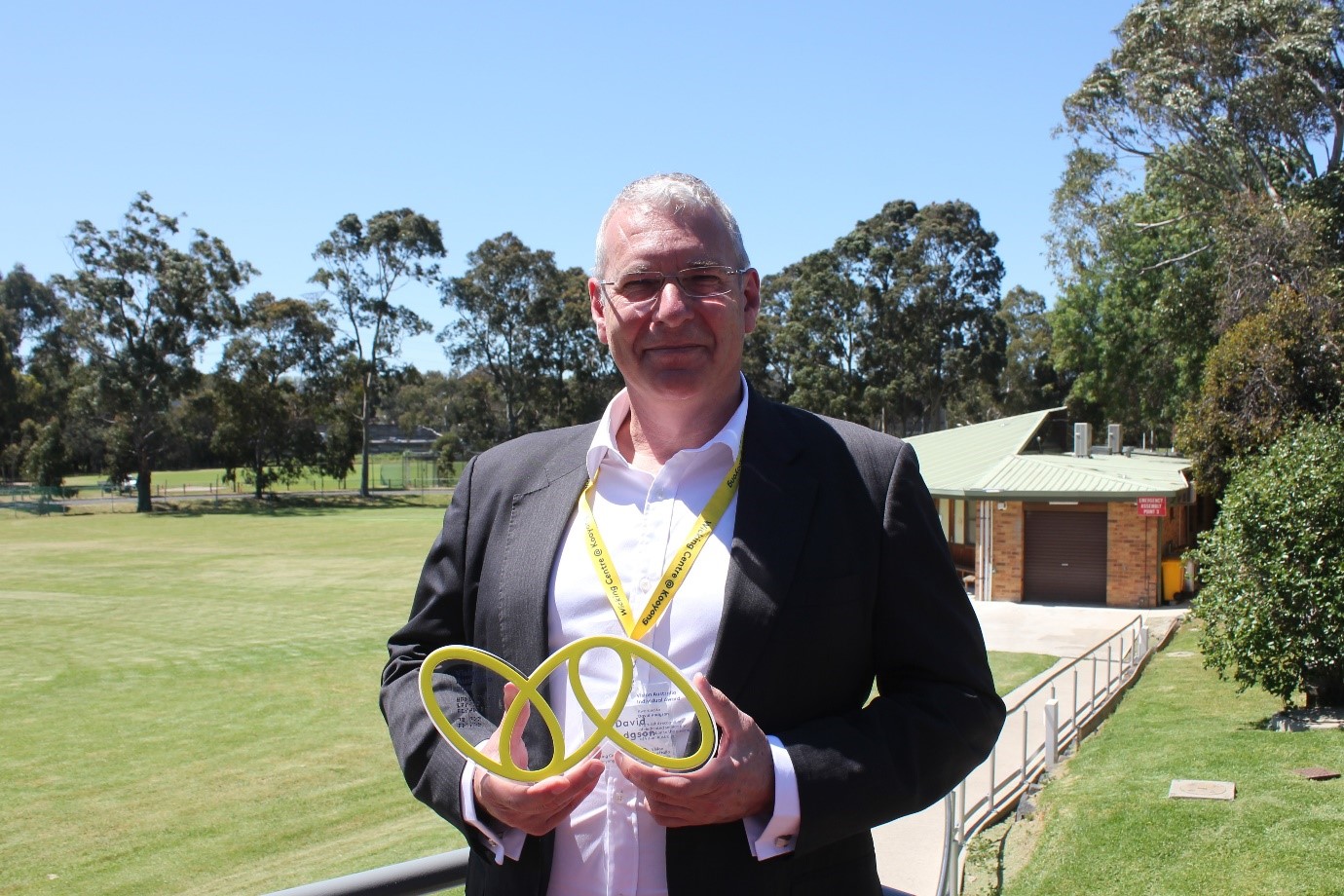 "VA Award winner David, holding his award which takes the shape of the VA logo of 3 yellow ovals linked together"