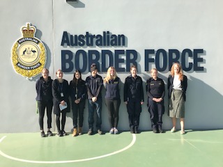 "Team members from both Seeing Eye Dogs and the Australian Border Force stand together in front of a wall with the Australian Border Force logo"
