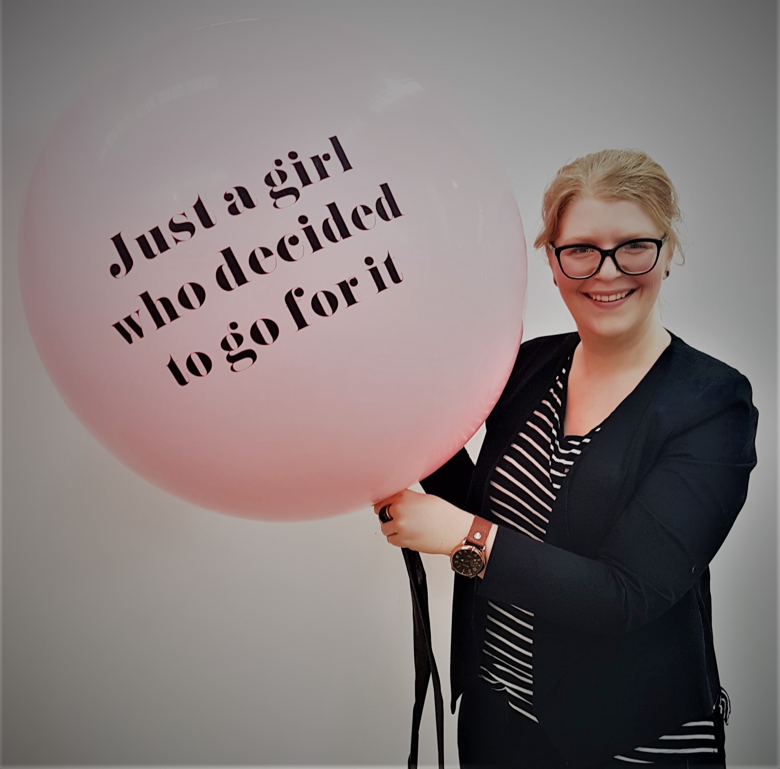 "Libby standing to the right of a pink balloon with the words "Just a girl who decided to go for it" written on it."