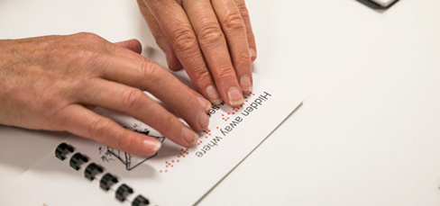 Pair of hands reading braille on a bound document