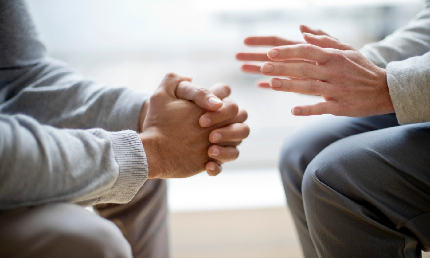 Two people having a difficult conversation, one with hands bunched together receiving feedback and the other with palms open giving feedback