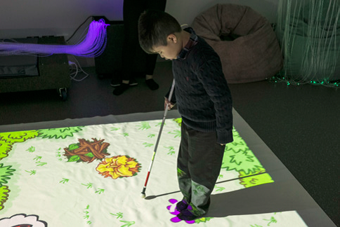 Child with white cane standing on the magic carpet in the sensory room