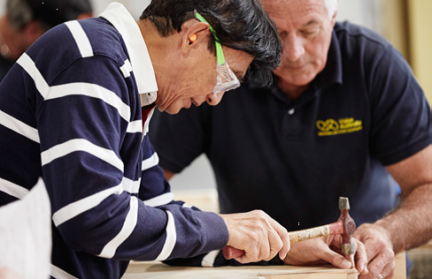 Man with protective goggles talking with Vision Australia woodwork instructor