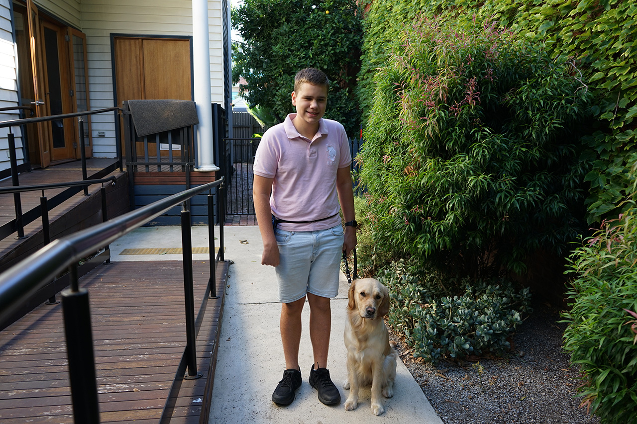 A teenage book stands outside with his yellow labrador Seeing Eye Dog