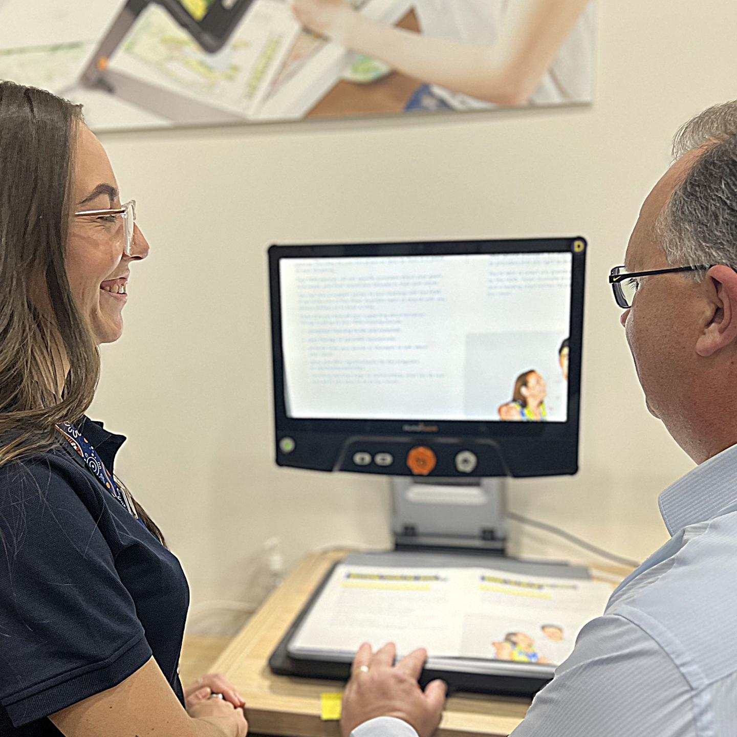 Vision Store team member and customer are looking towards a screen that has enlarged text