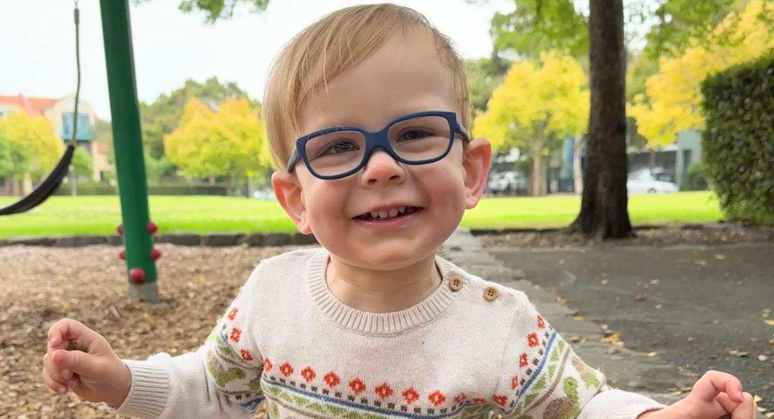 Finn is wearing glasses and smiling at the camera. He is standing in front of a swingset.