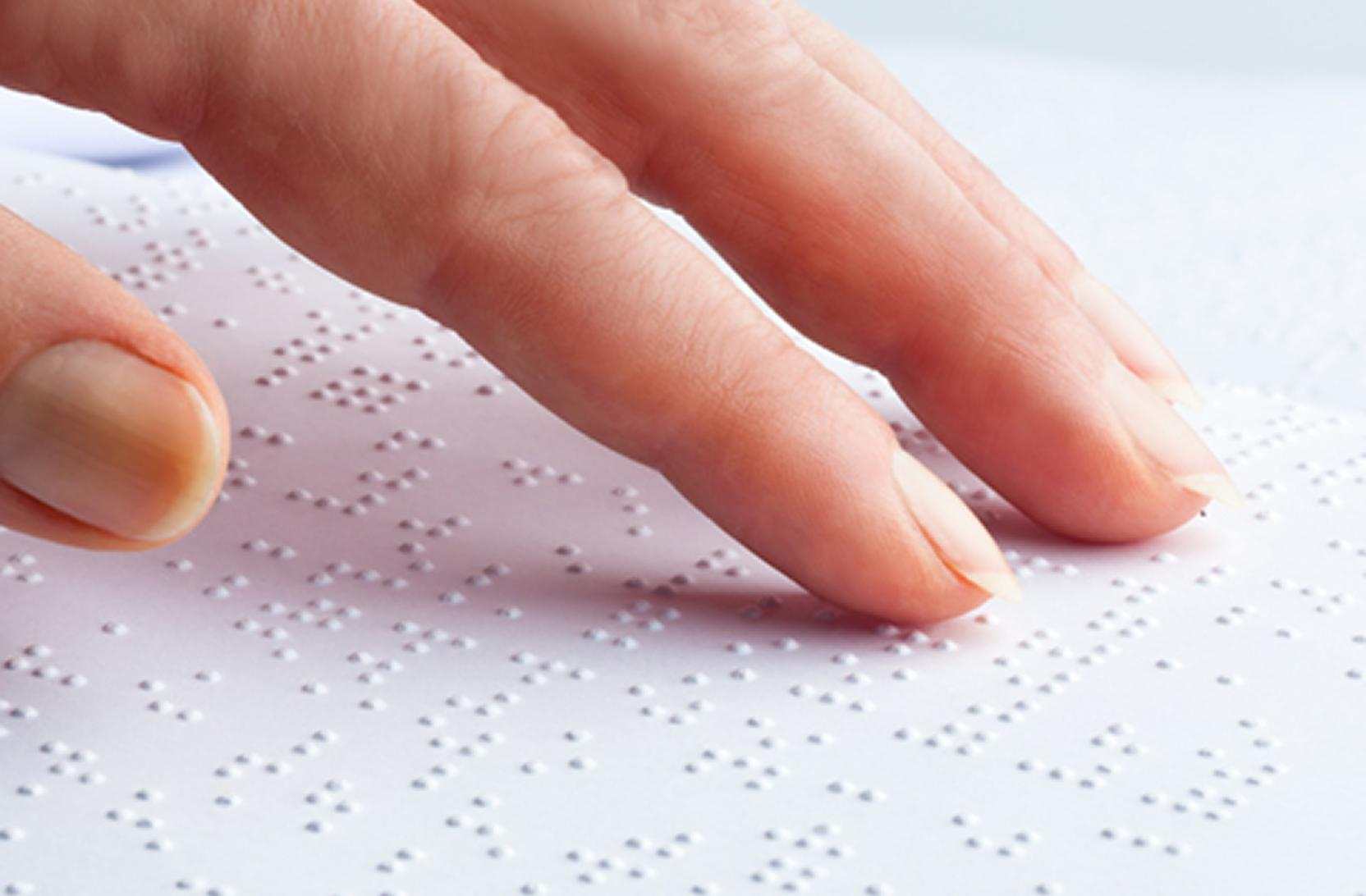 A close up of an adult hand reading some braille text