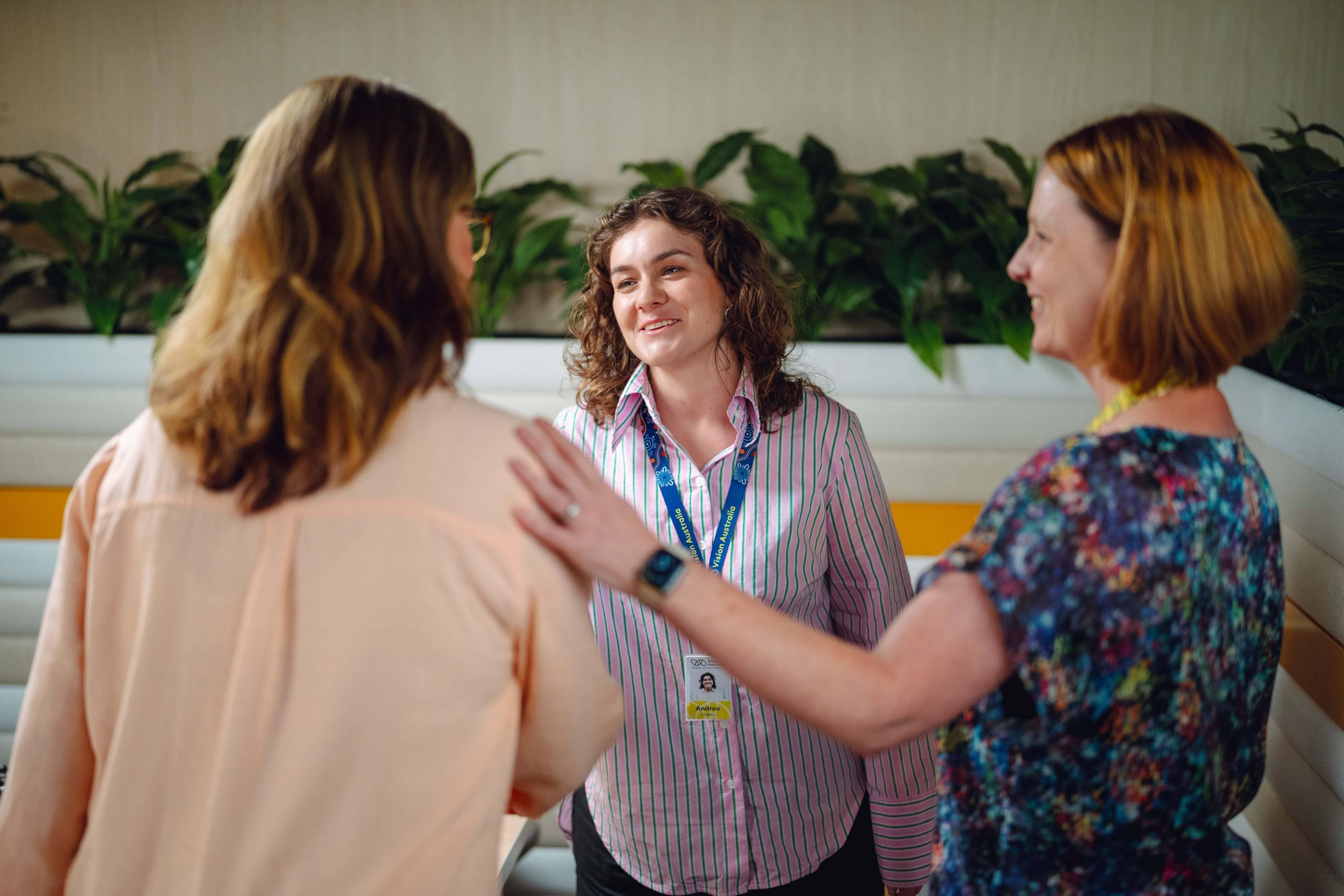Two female service providers standing with a female client, all smiling and engaged in a group setting.
