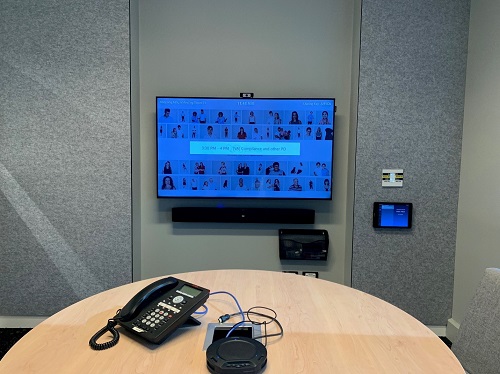 A large TV screen with teleconferencing equipment on a table in front of it